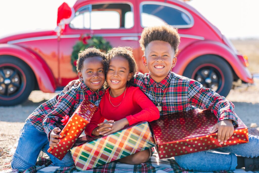 Three kids smiling for Christmas mini session photoshoot in presents and car in Rosamond, California