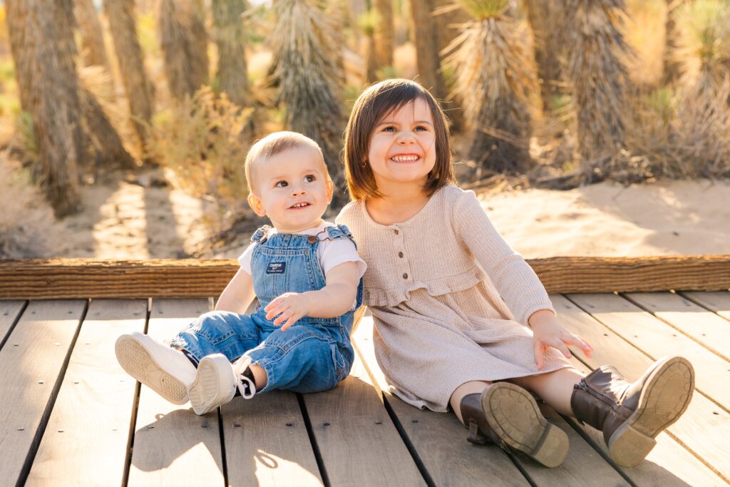 Siblings smiling during golden hour lighting in front of Joshua trees during family photoshoot in Lancaster, California