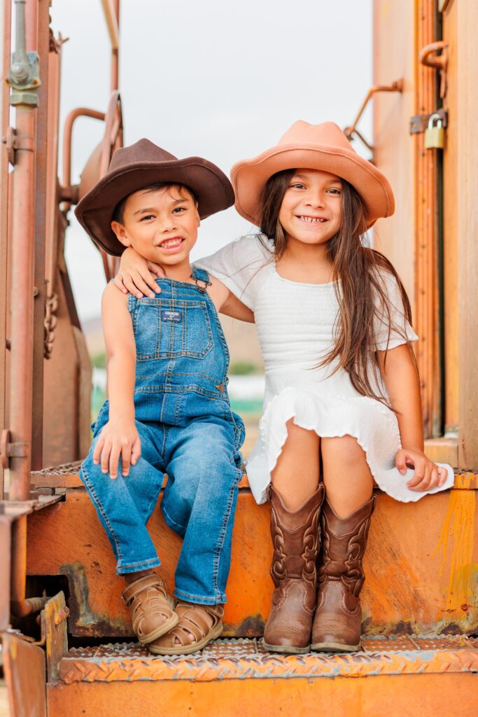 Two kids dressed in western theme outfits sitting on caboose during family photoshoot near Santa Clarita, California