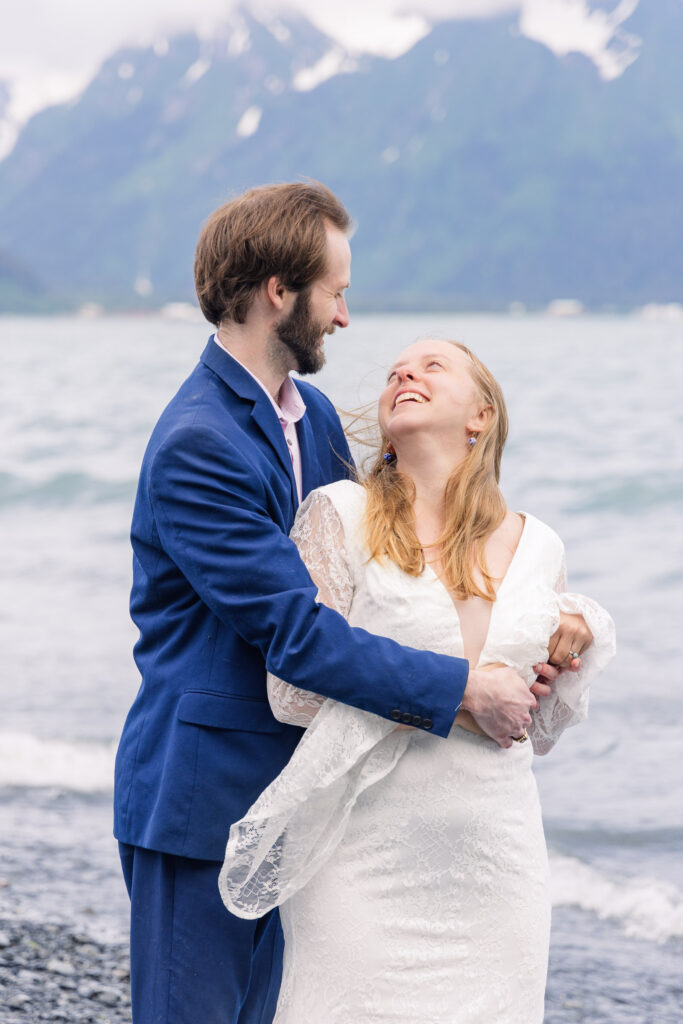 Wedding couple smiles on beach in front of mountains in Seward, Alaska during adventure elopement