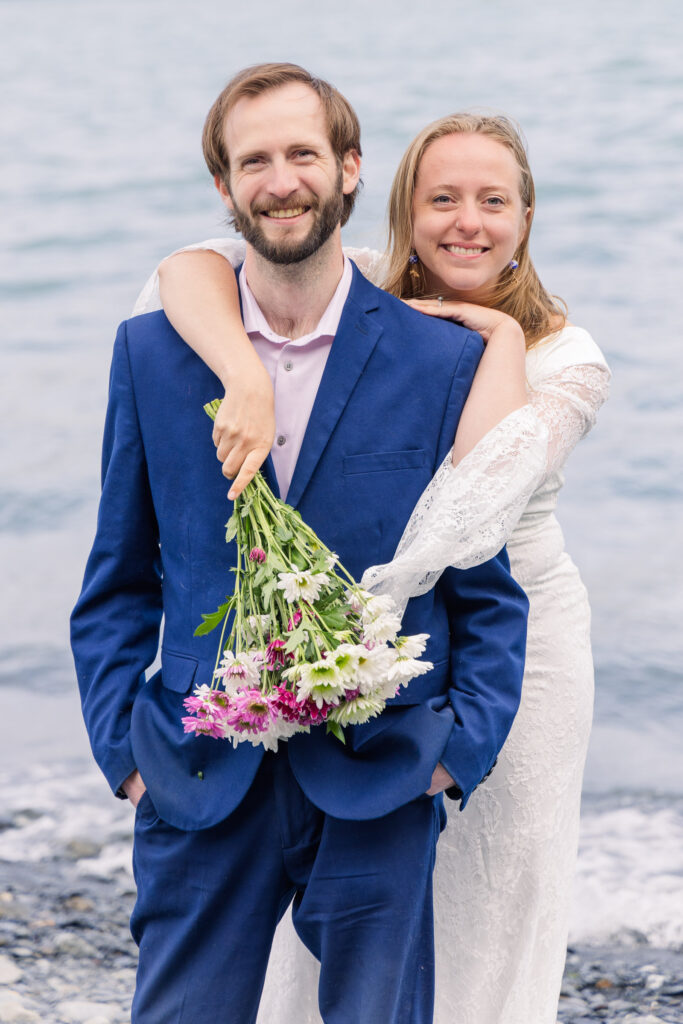 Wedding couple smiles on beach in front of mountains in Seward, Alaska during adventure elopement