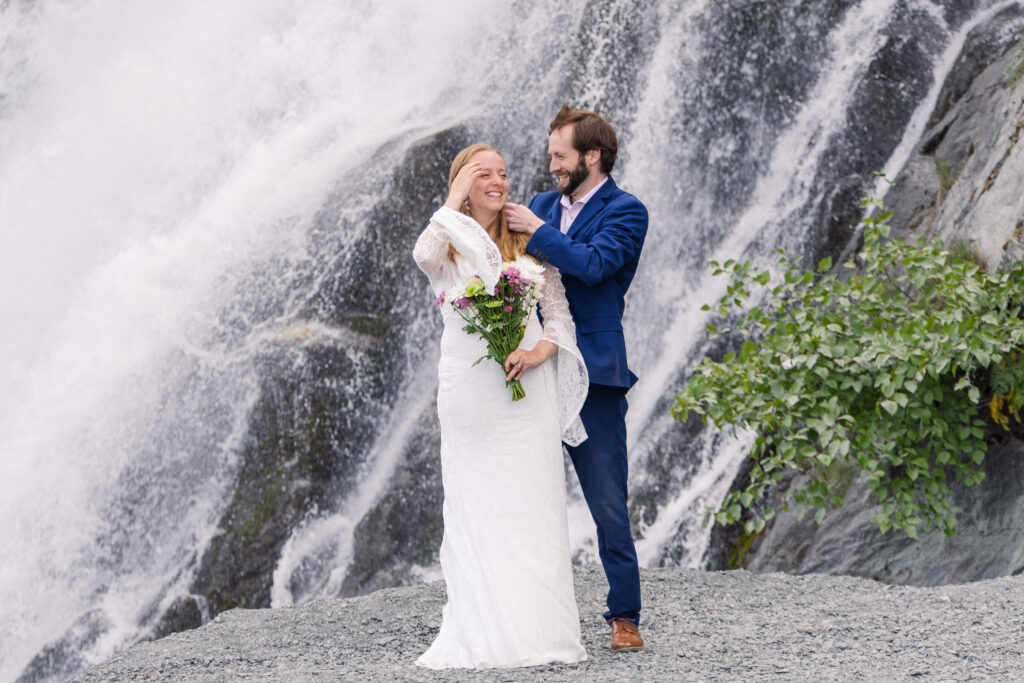 Bride and groom celebrate in front of waterfall during elopement in Seward, Alaska