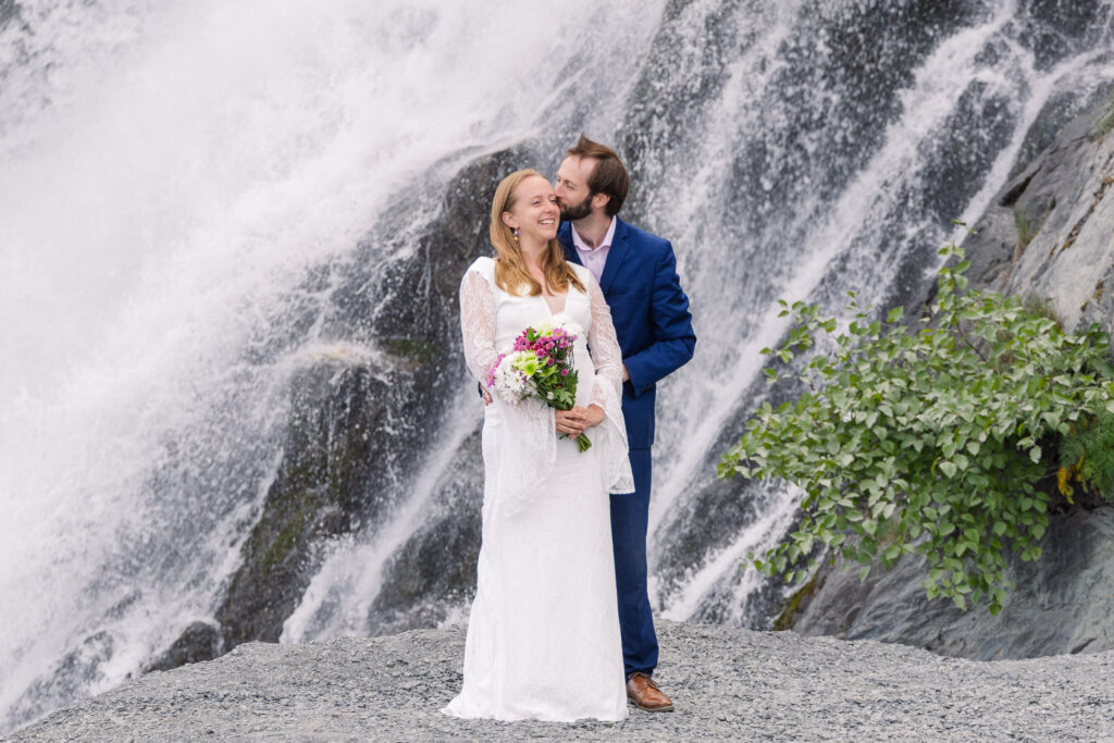 Bride and groom celebrate in front of waterfall during elopement in Seward, Alaska