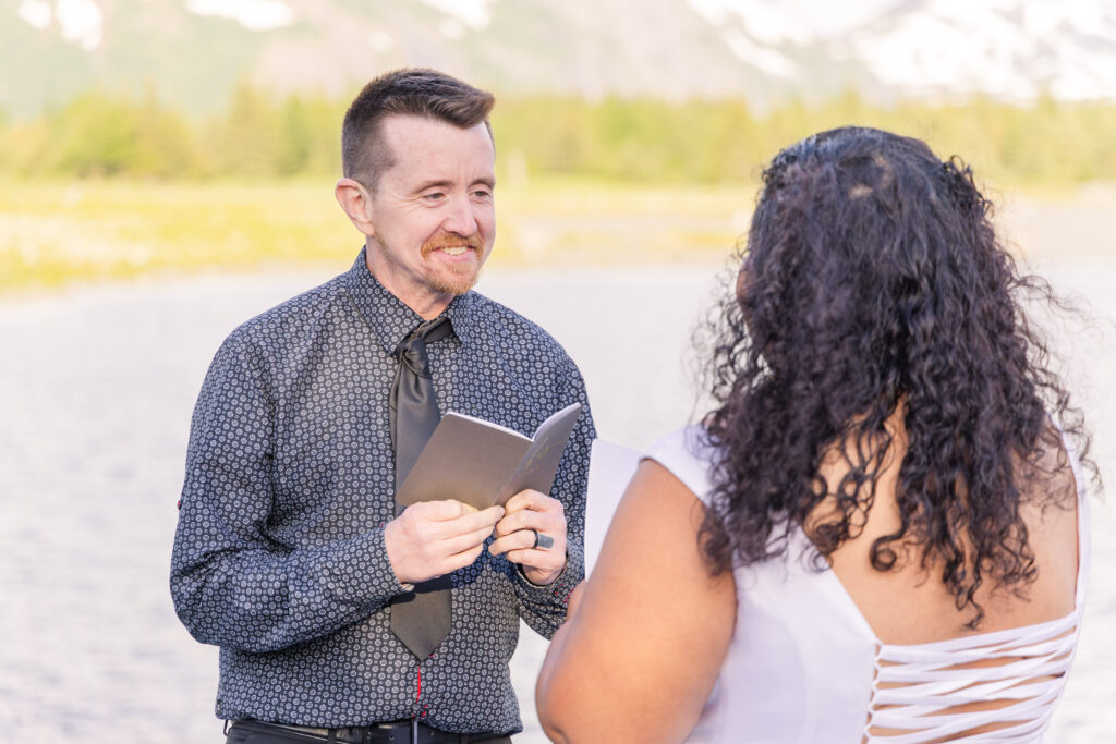 Couple exchanging wedding vows at scenic elopement in front of glacier, mountain, and lake in Whittier, Alaska