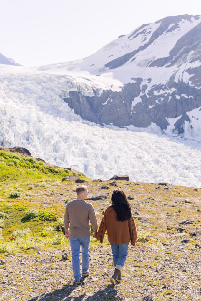 Couple holds hands and walks from helicopter to glacier viewpoint in Alaska.