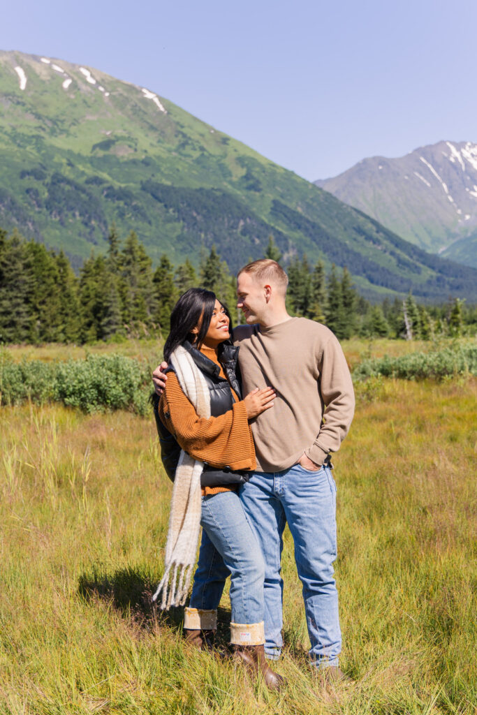 Couple looks lovingly into each other's eyes in front of scenic mountains near Girdwood, Alaska, after getting engaged.