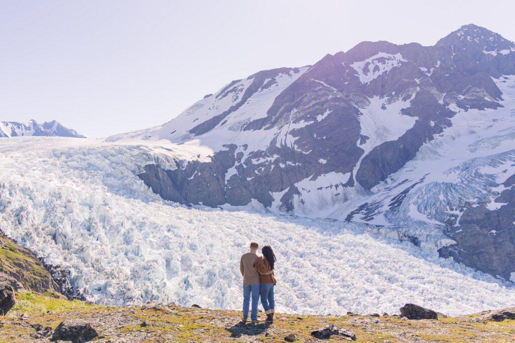 Couple holds each other while overlooking massive glacier after helicopter landing in Alaska.