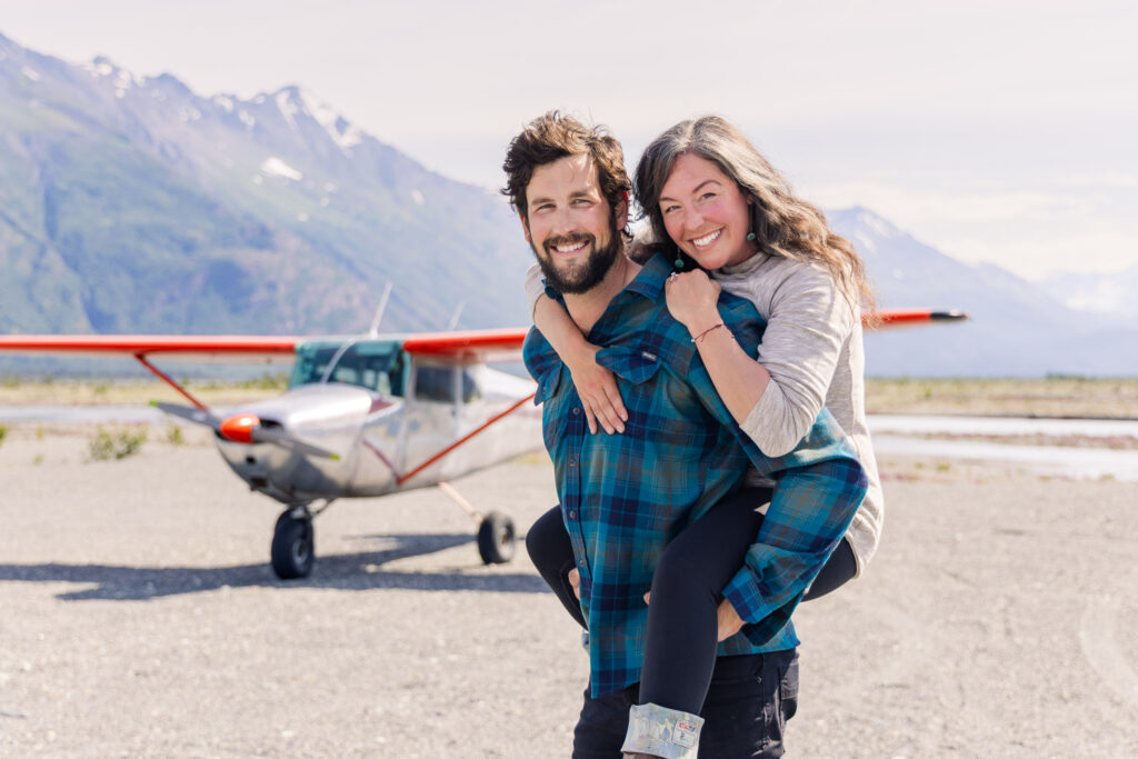 Couple poses in front of Cessna airplane in Alaskan backcountry