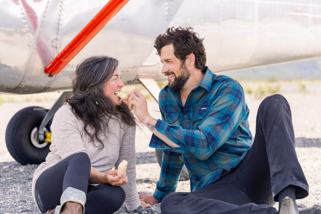 Couple feeds each other dessert in front of their airplane after getting engaged in the Alaskan backcountry