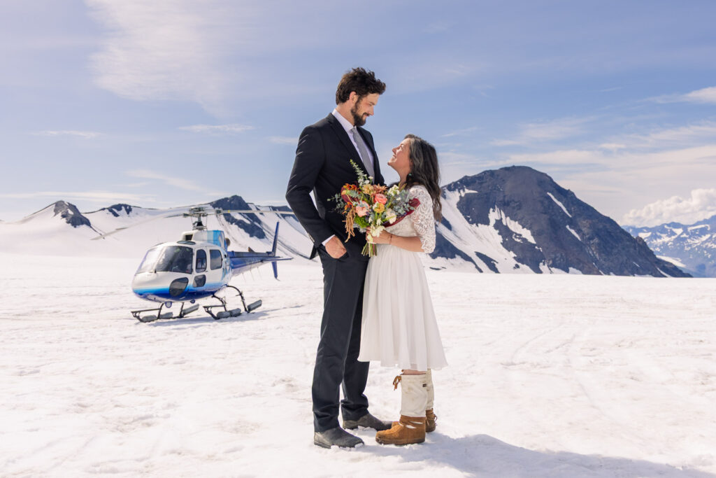 Eloping couple in front of helicopter on snowy glacier during Alaska elopement