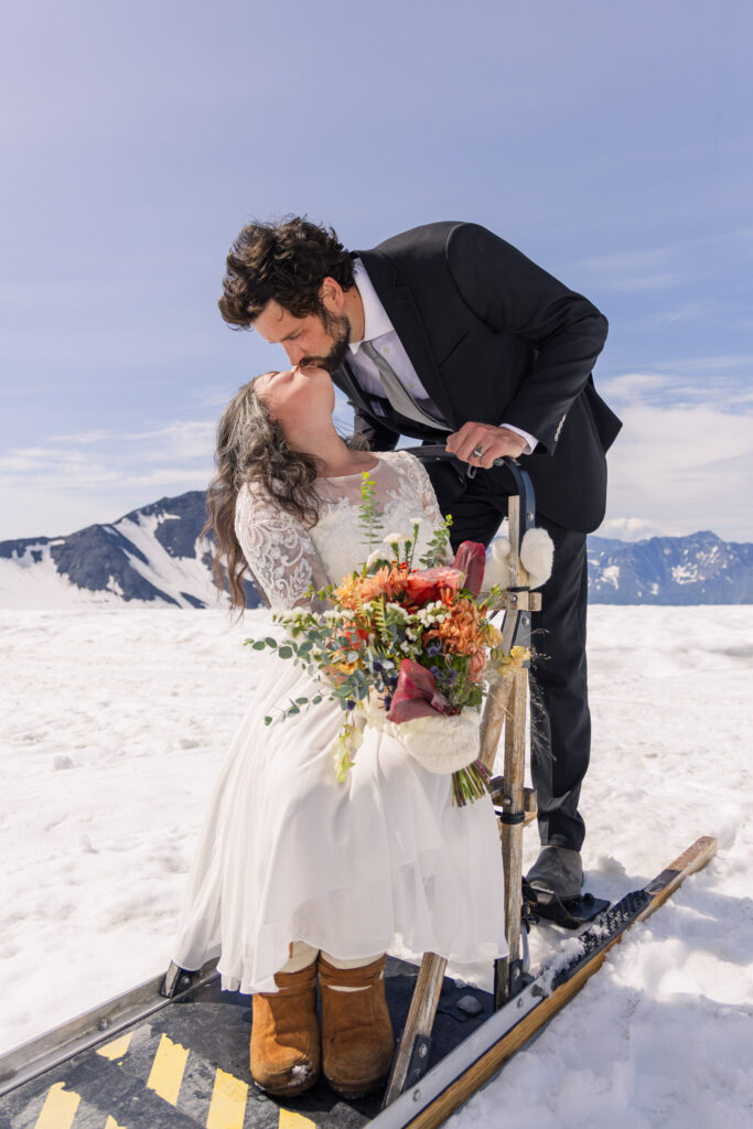 Couple kissing during portraits with dogsled during Alaska dogsledding elopement