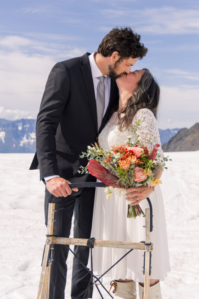 Couple kissing during portraits with dogsled during Alaska dogsledding elopement