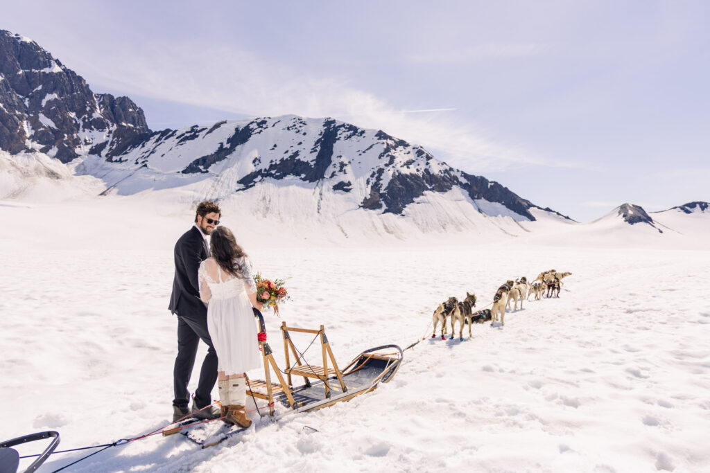 Bride and groom with dogsled husky team during Alaska dogsledding elopement on glacier