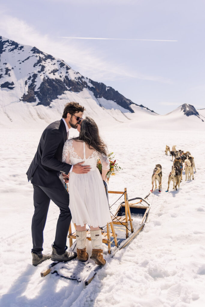 Bride and groom kissing behind dogsled team during Alaska dogsledding elopement on glacier