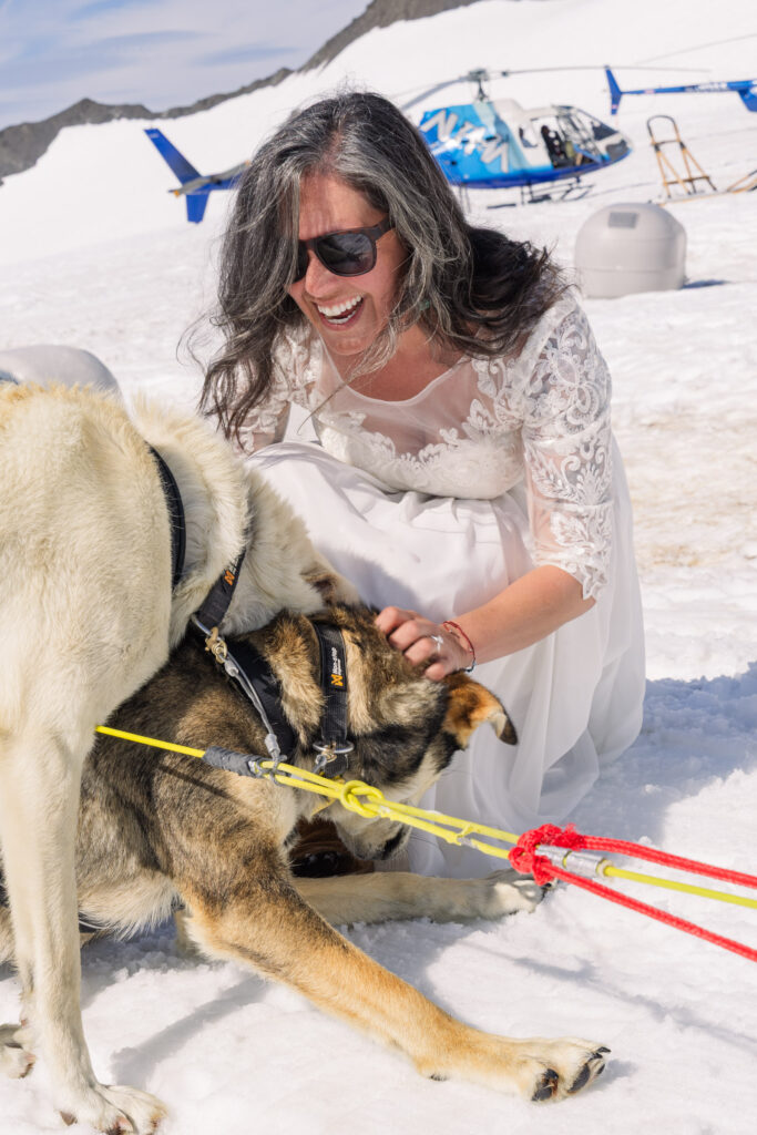 Bride playing with sled dogs at glacier dogsled camp during Alaska elopement