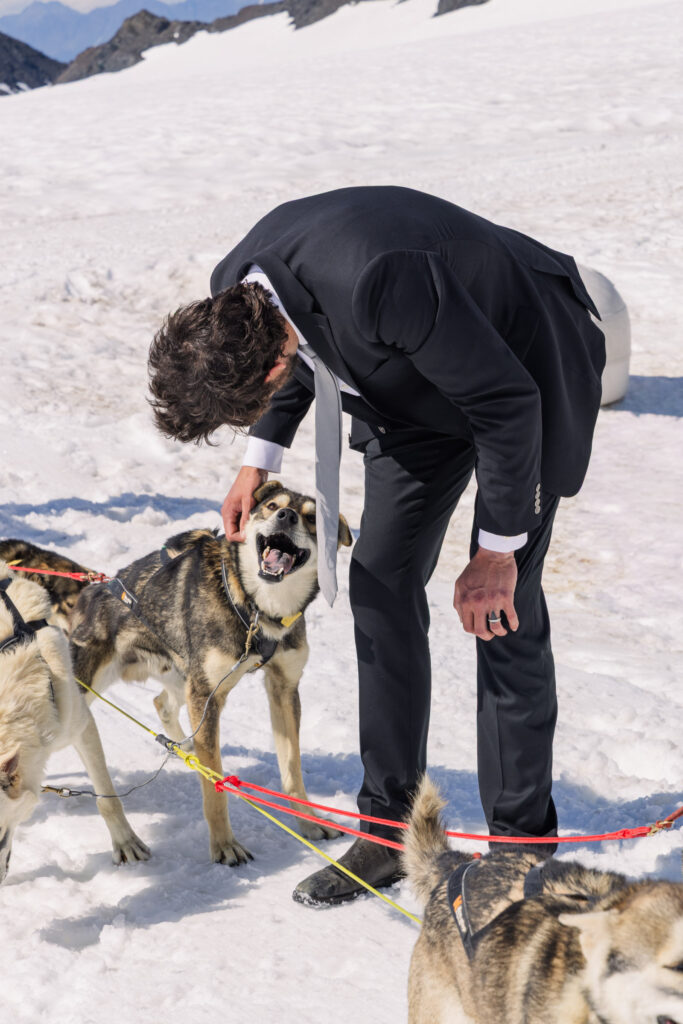 Groom playing with sled dogs at glacier dogsled camp during Alaska elopement