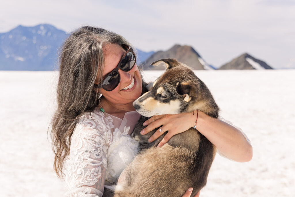 Bride playing with husky puppy at glacier dogsled camp during Alaska elopement