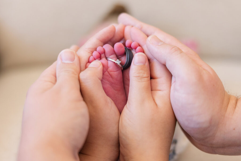 close-up detail of wedding rings on baby's feet with parent hands holding the feet
