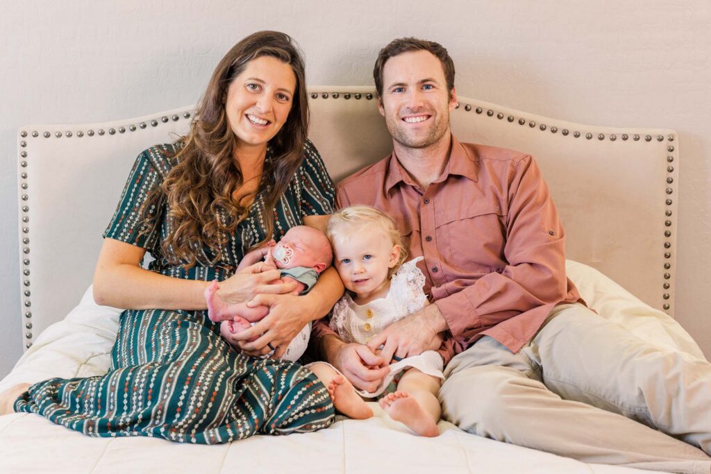 family on bed with newborn baby and toddler