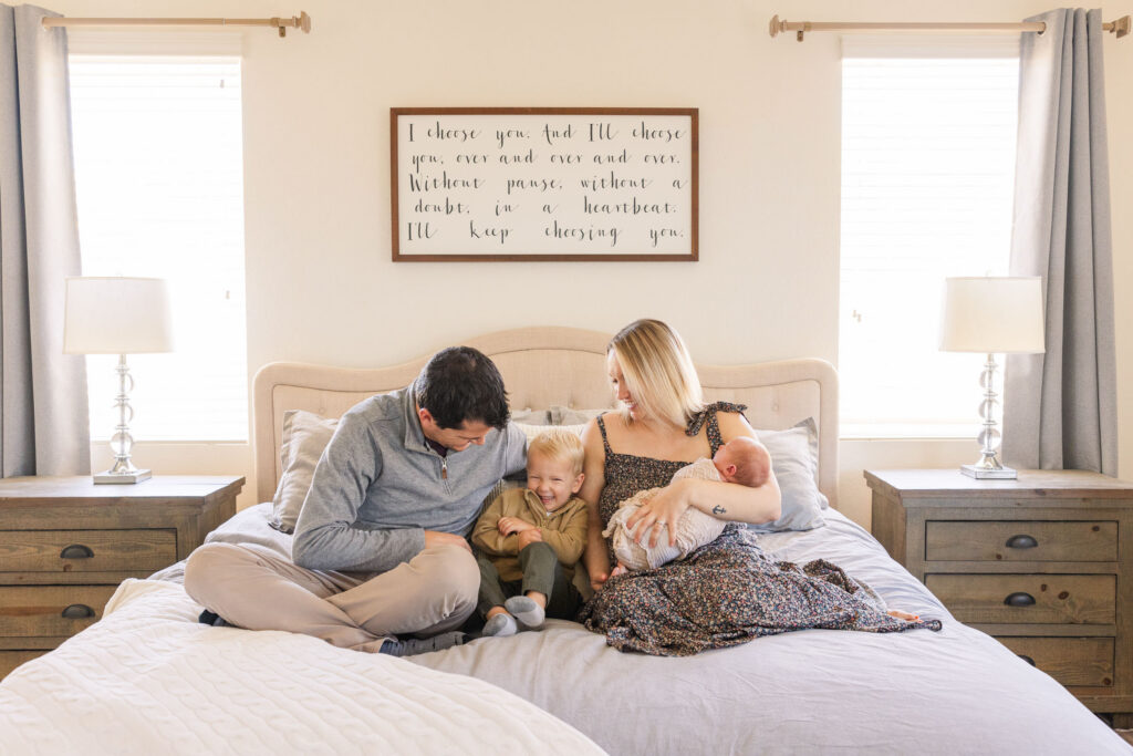 family on bed with newborn baby and laughing toddler in lifestyle session