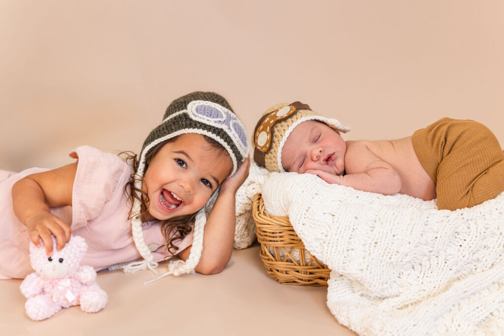 toddler and infant in matching pilot hats and goggles during studio photoshoot