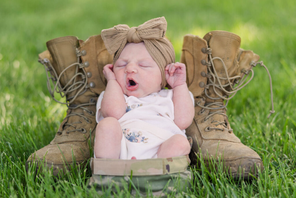 newborn baby sitting in military uniform hat next to military boots