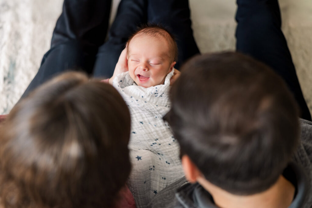 parents looking down at smiling newborn baby they are holding during lifestyle newborn session