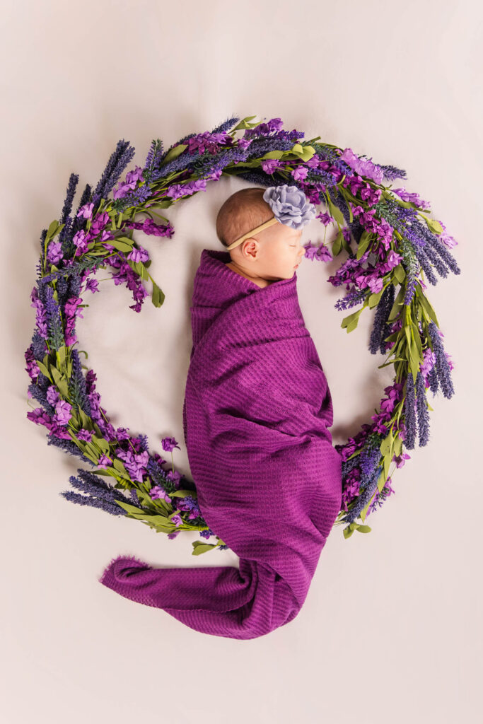 top-down view of newborn girl with purple flower wreath and purple bow