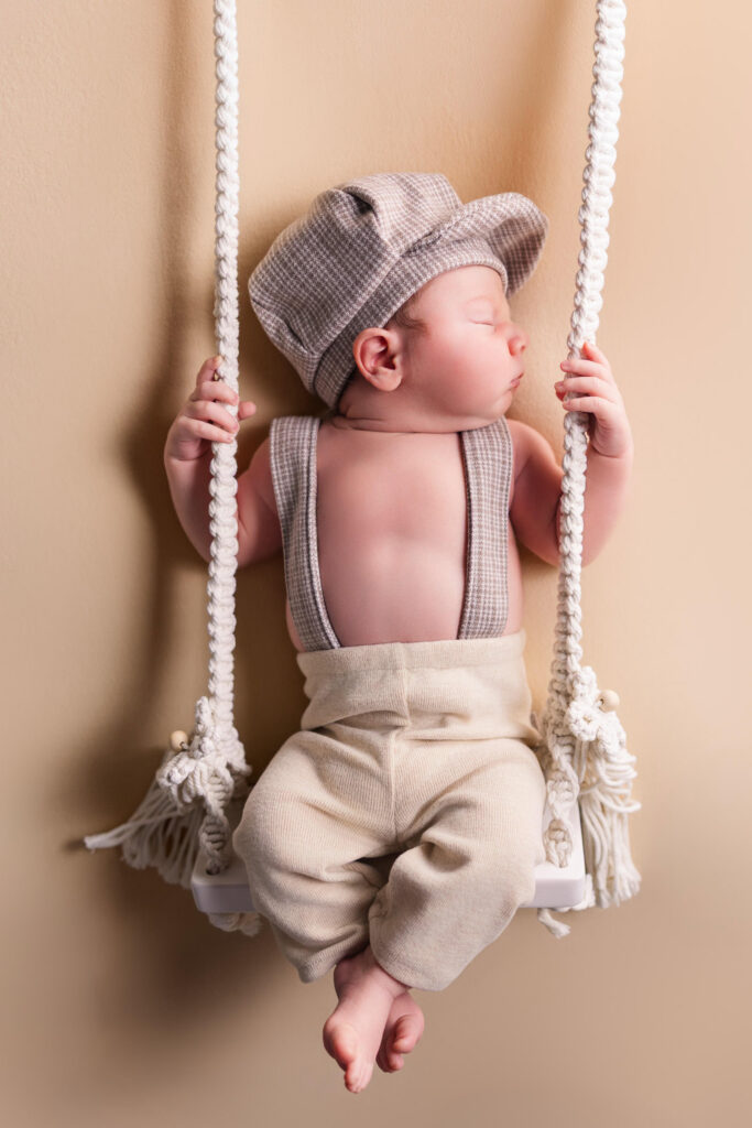 newborn on swing wearing gentleman outfit in studio newborn photography session