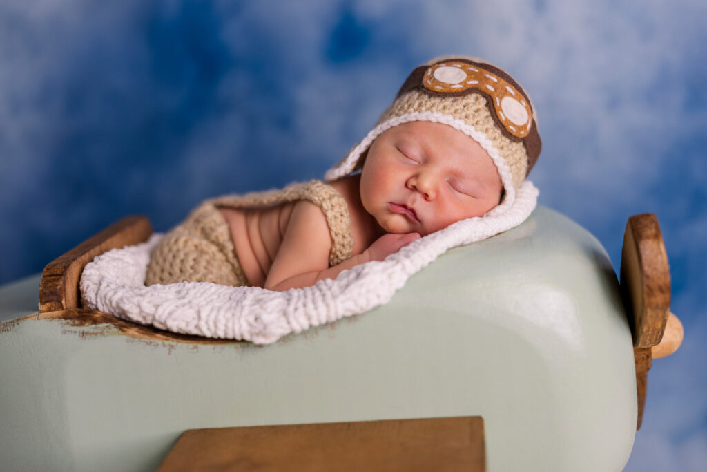 newborn wearing pilot helmet and goggles in wooden model plane during studio newborn session