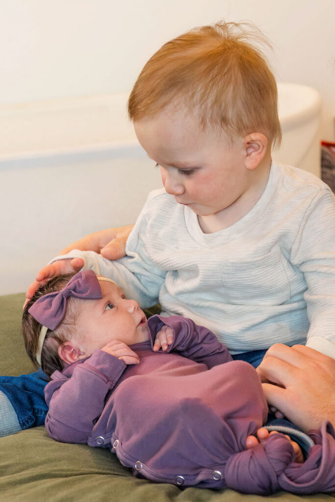 toddler looking down at newborn sister during lifestyle sibling photos