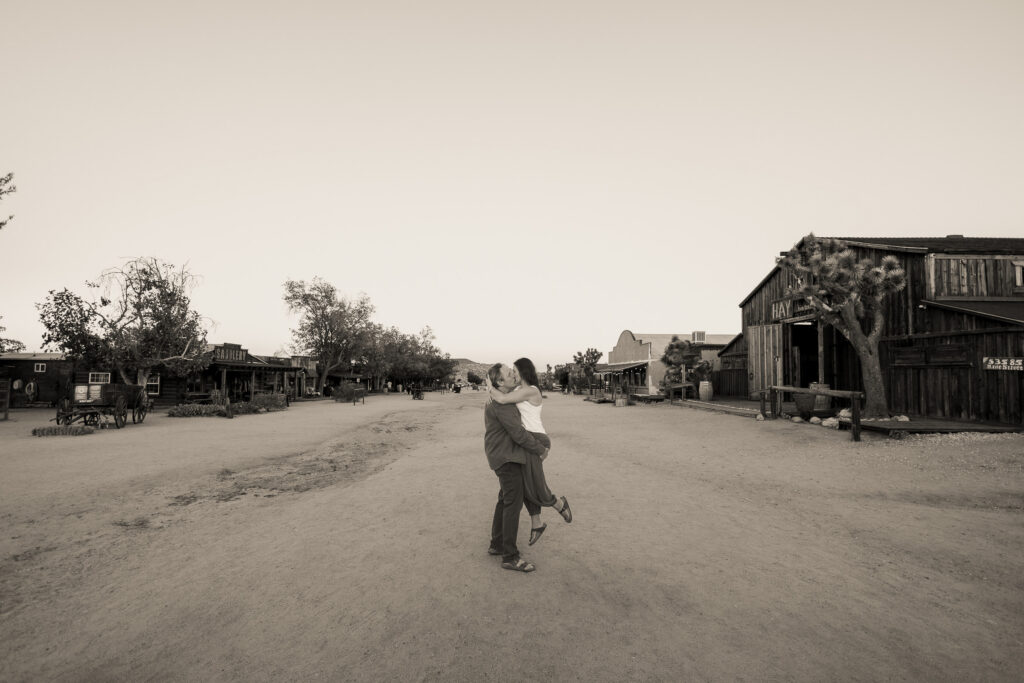 David lifting Lisa for a kiss in the middle of Mane Street in historic California Pioneertown, in black and white.