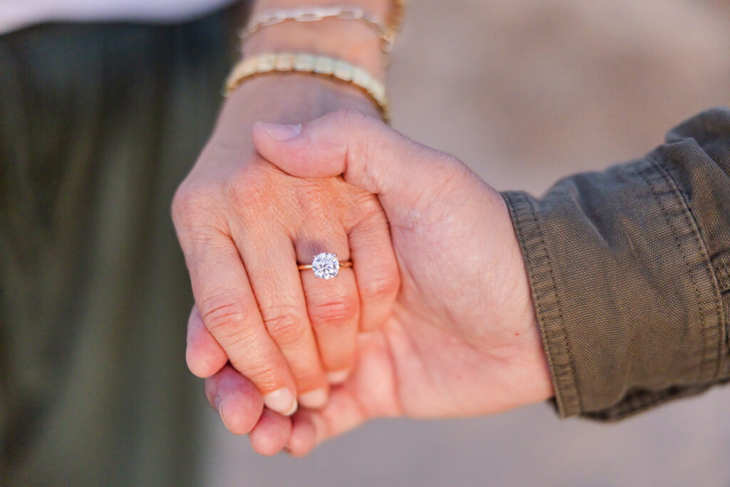 Close-up of David and Lisa holding hands, showing Lisa's engagement ring after their surprise proposal.