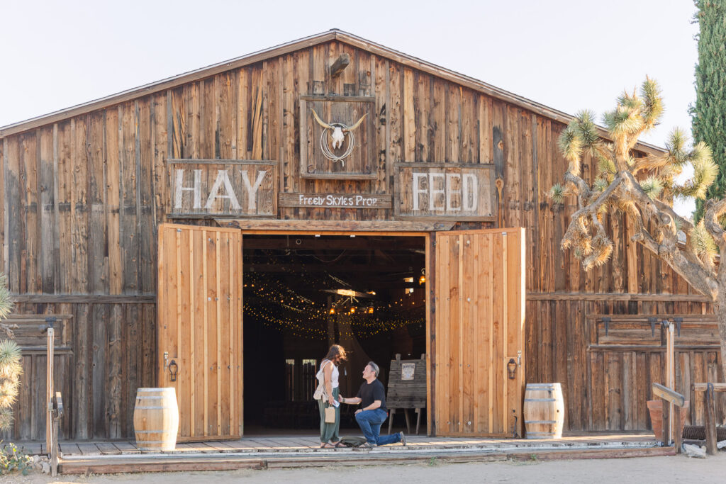 David proposing to Lisa on porch of Pioneertown Soundstage with its wooden facade and Hay & Feed sign.