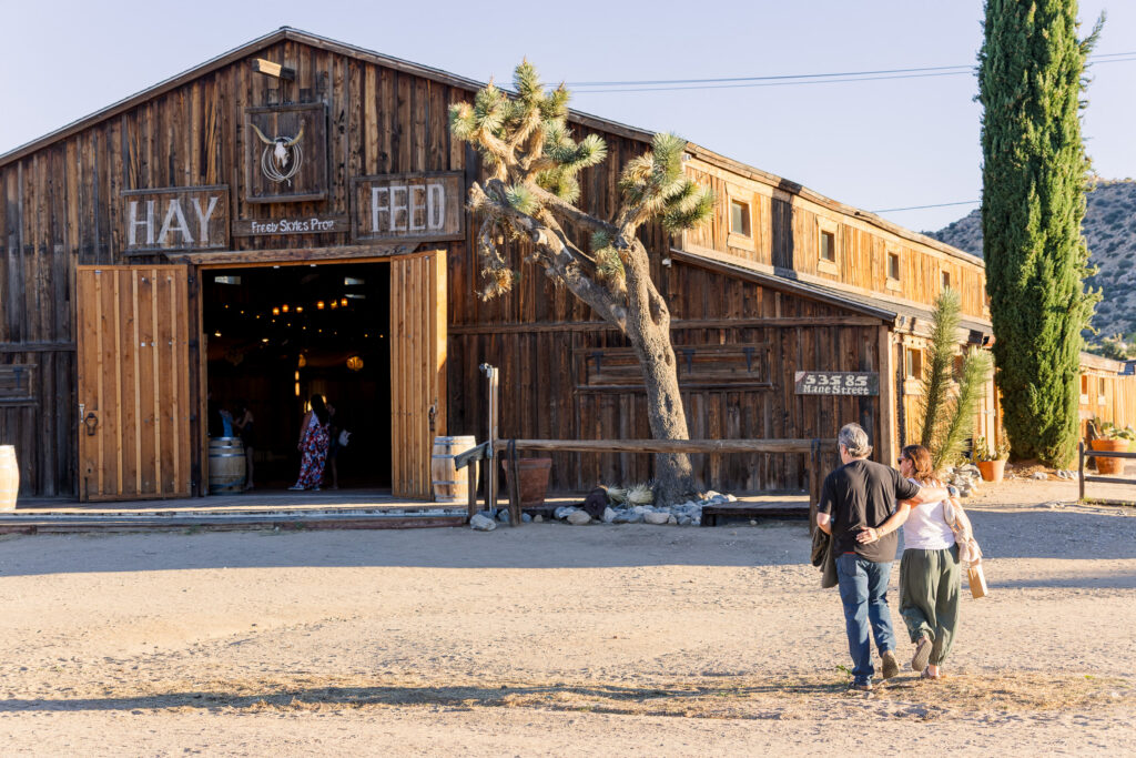 Couple walking towards rustic wooden storefront along Pioneertown's historic Mane Street in the California desert.