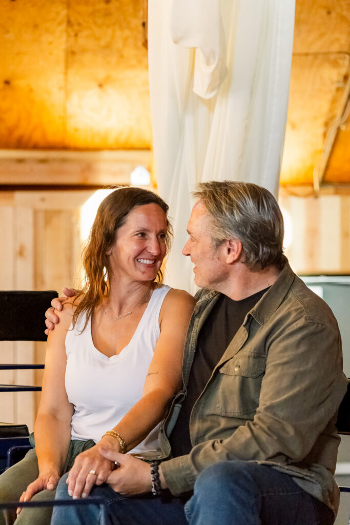 David and Lisa smiling at each other while seated in a wagon inside the rustic Pioneertown Soundstage.