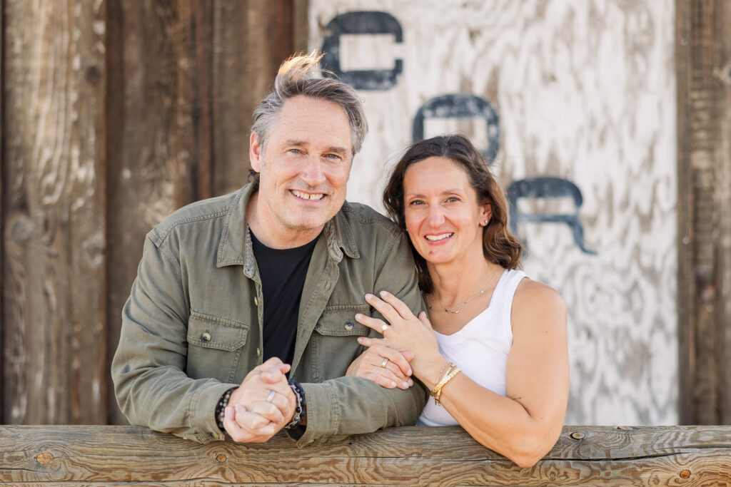 David and Lisa leaning together against a wooden fence during their desert engagement portraits.