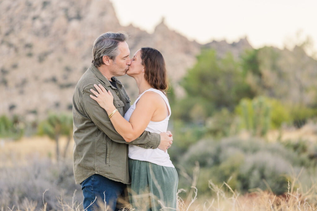David and Lisa kissing among desert shrubs during their golden-hour engagement session near Joshua Tree.