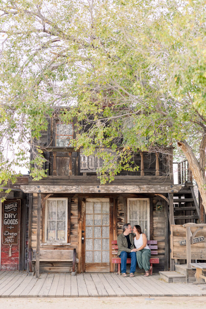 Newly engaged couple cuddled up on wooden bench outside Pioneertown Hotel.
