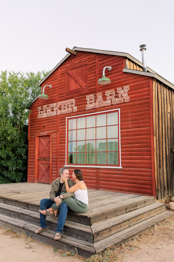 David and Lisa sitting together outside a weathered red wooden storefront along Mane Street.