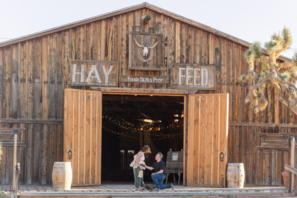 David kneeling to propose to Lisa outside the Pioneertown Soundstage, beneath the historic Hay & Feed sign.